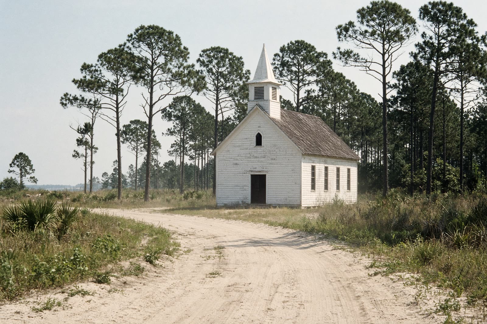 A small white wooden church at the end of a sandy road.